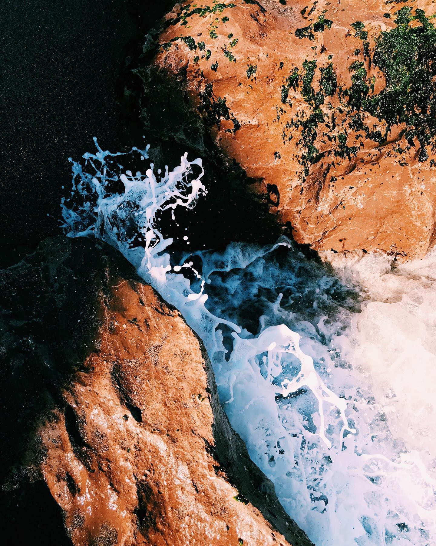 Olas rompiendo entre rocas de tonos cálidos